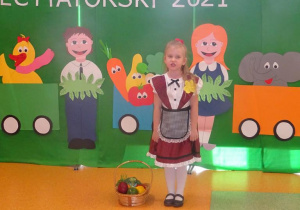 Dziewczynka recytuje wiersz, po jej prawej stronie leży koszyk z warzywami.